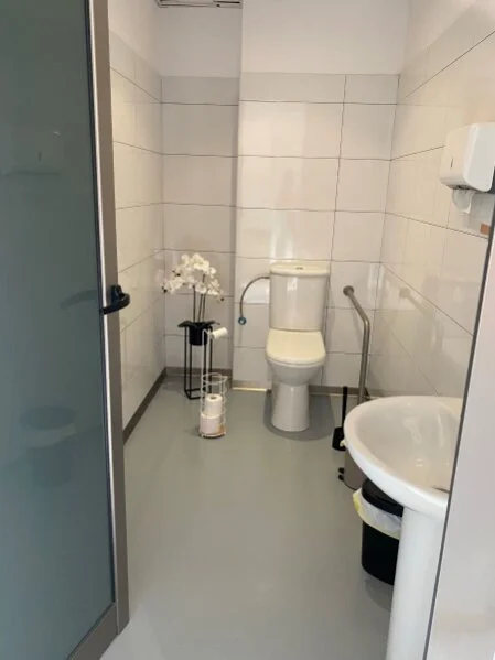 Barrierefreie Patiententoilette der Inselproktologie Mallorca mit Haltegriffen, heller Ausstattung und einer Blume als freundlicher Akzent.
